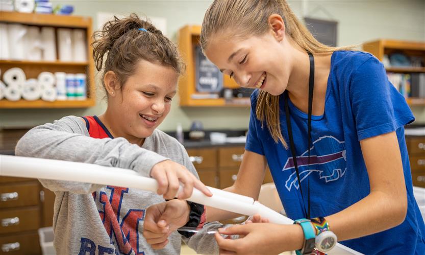 Two students laugh while building a mini rollercoaster track